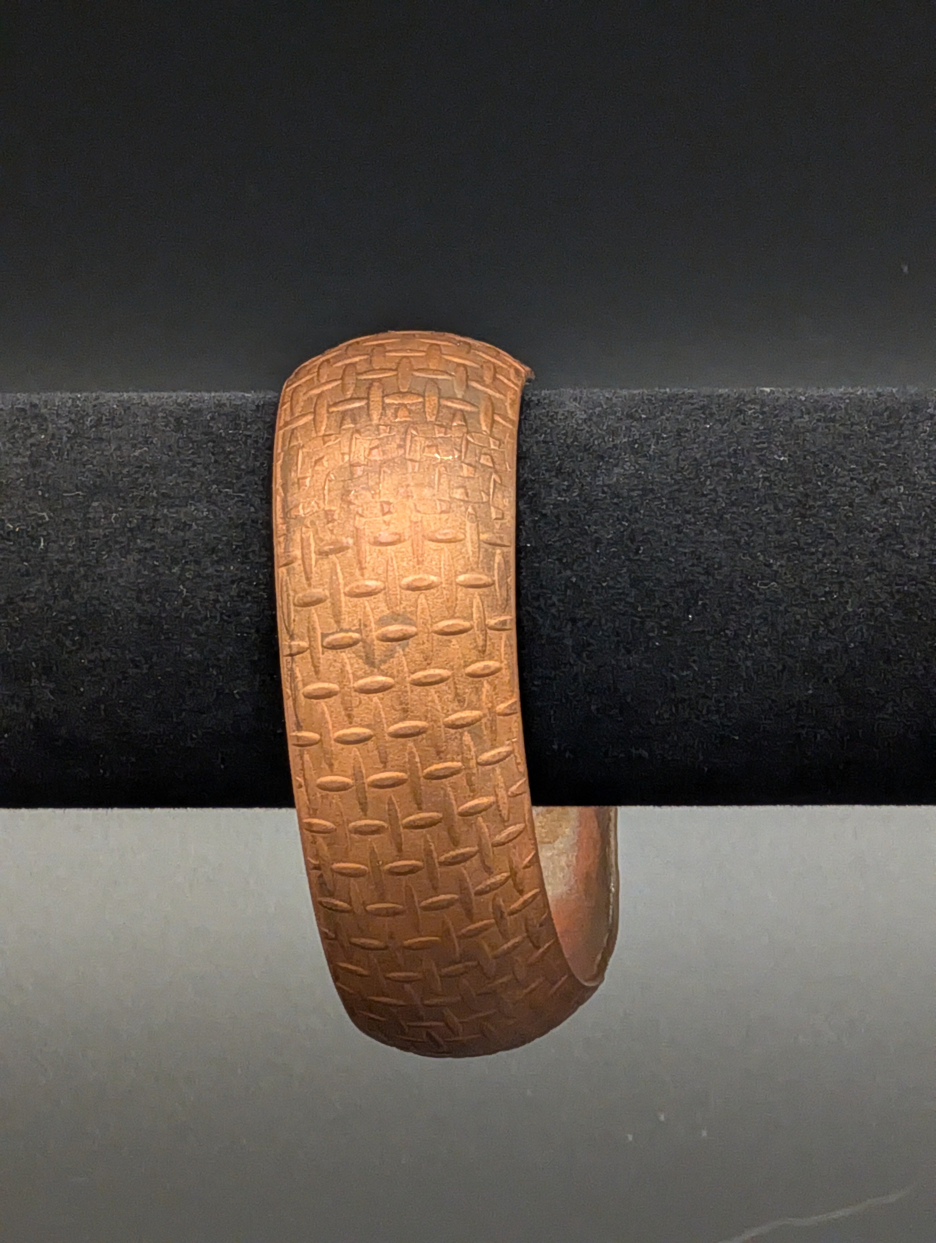 A curved copper cuff with a pattern similar to metal plate applied to the exterior.