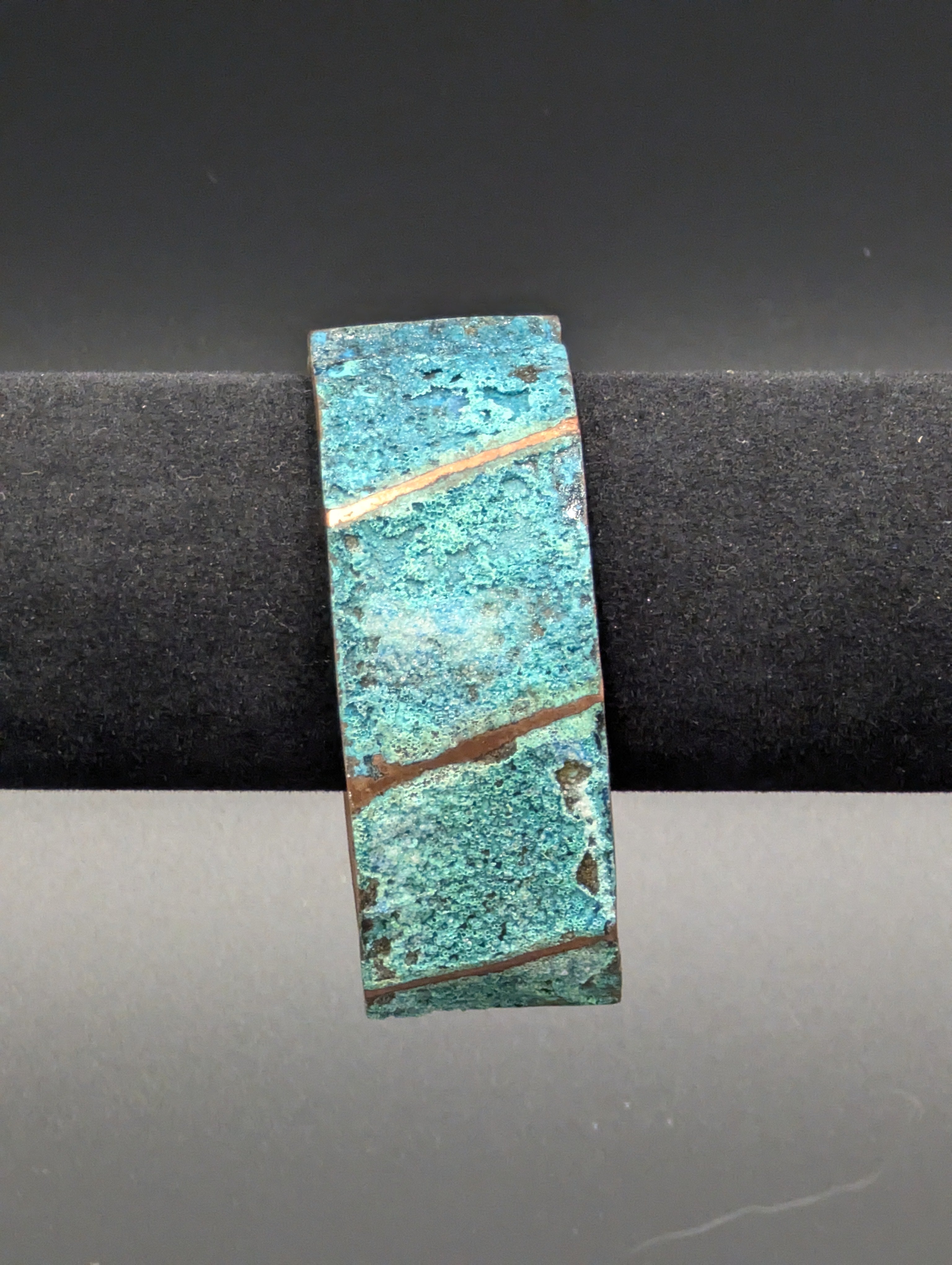 A copper cuff consisting of folded ridges and the low areas are covered in a rugged blue patina.