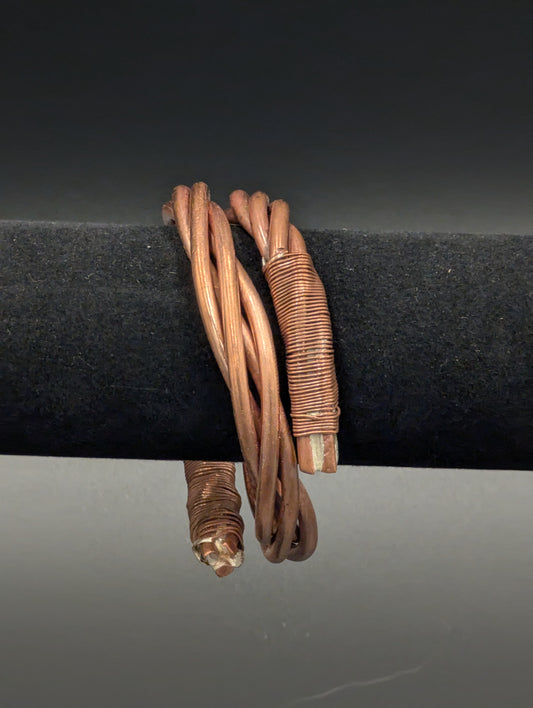 Copper bracelet displayed on black velvet. The bracelet consists of several wires twisted together. The ends of the cuff are then wrapped in a smaller wire.