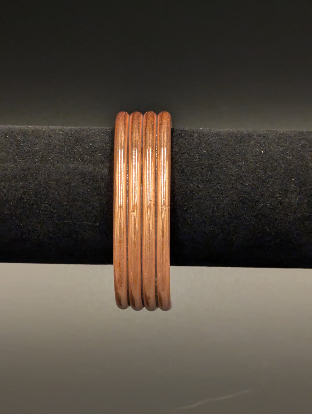 A copper cuff bracelet sitting on a black velvet display. The view is edge on and the bracelet consists of 4 wires connected side by side for a simple yet elegant design.