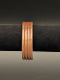 A copper cuff bracelet sitting on a black velvet display. The view is edge on and the bracelet consists of 4 wires connected side by side for a simple yet elegant design.