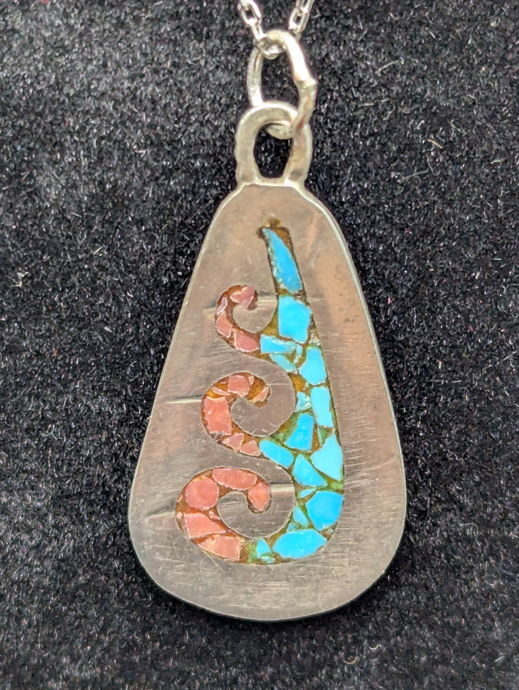 Silver pendant with turquoise and coral inlay on a dark textured background