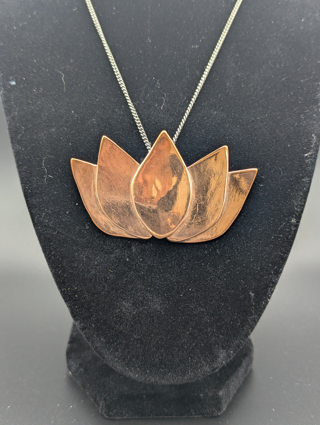 Copper lotus flower necklace on a black stand