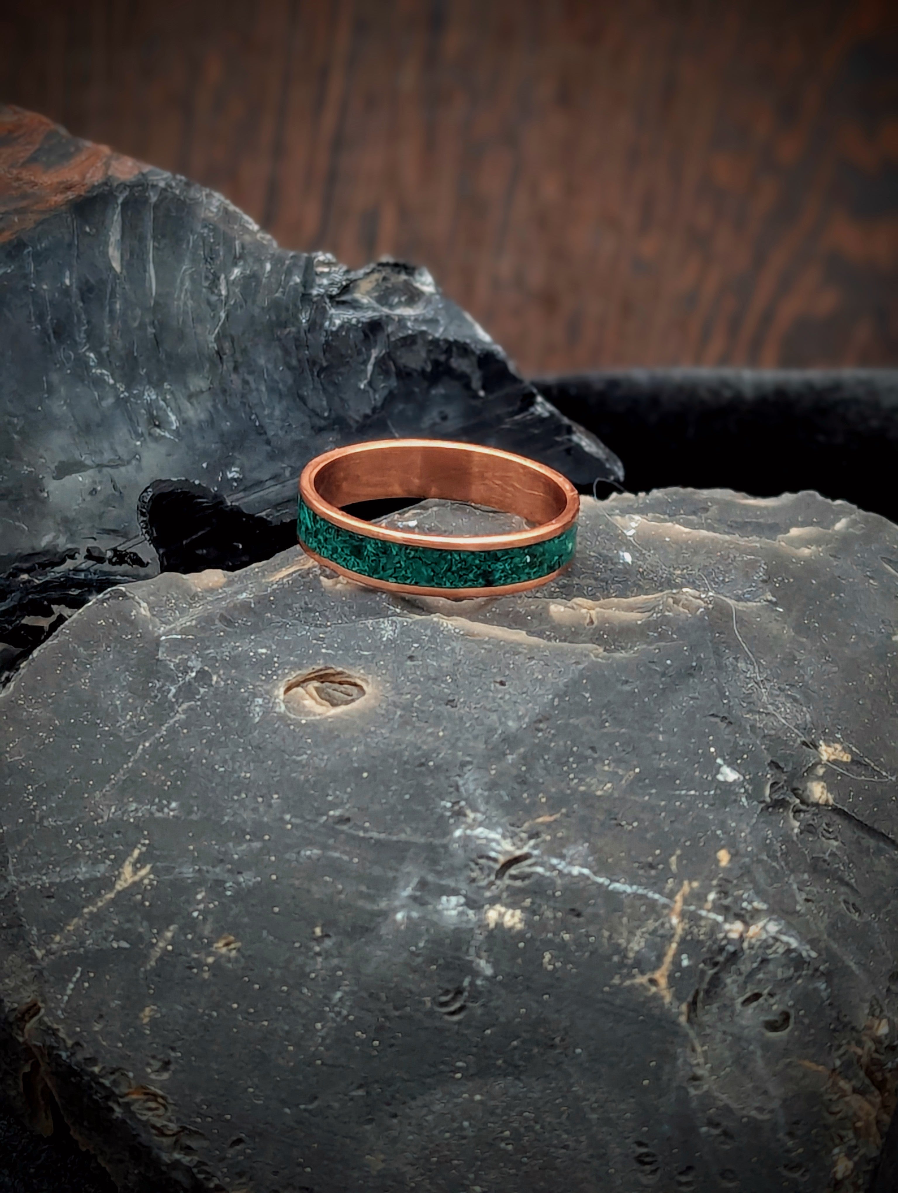 Copper ring with green malachite inlay on a textured stone surface