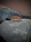 Copper ring with turquoise inlay on a dark stone surface