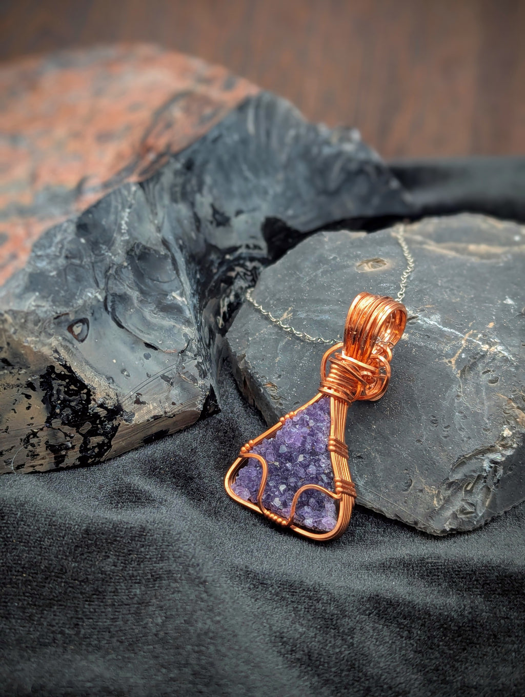 Purple stone pendant with copper wire wrapping on a dark stone surface