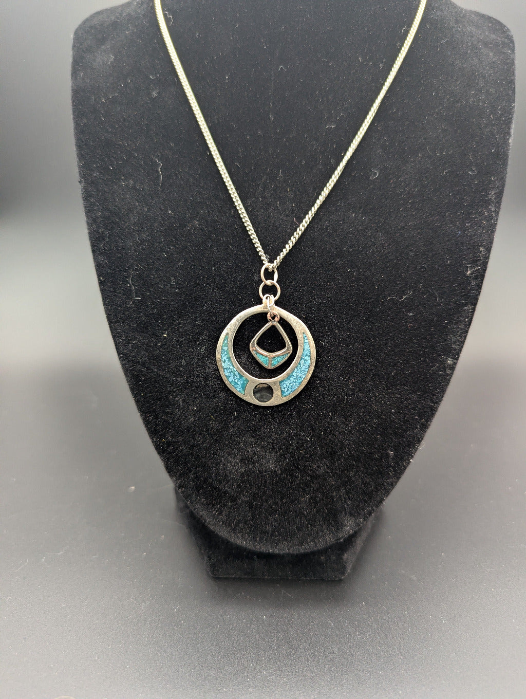 Necklace with a circular pendant featuring turquoise stones on a black stand.