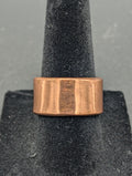 Copper ring on a gray stand with a plain background. This ring has no texture, but instead lets the natural shine of raw copper show.