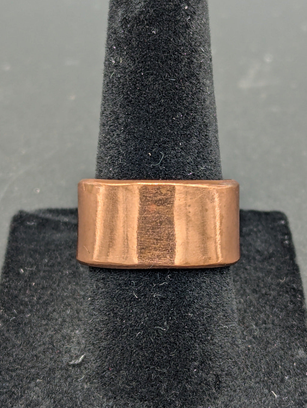 Copper ring on a gray stand with a plain background. This ring has no texture, but instead lets the natural shine of raw copper show.