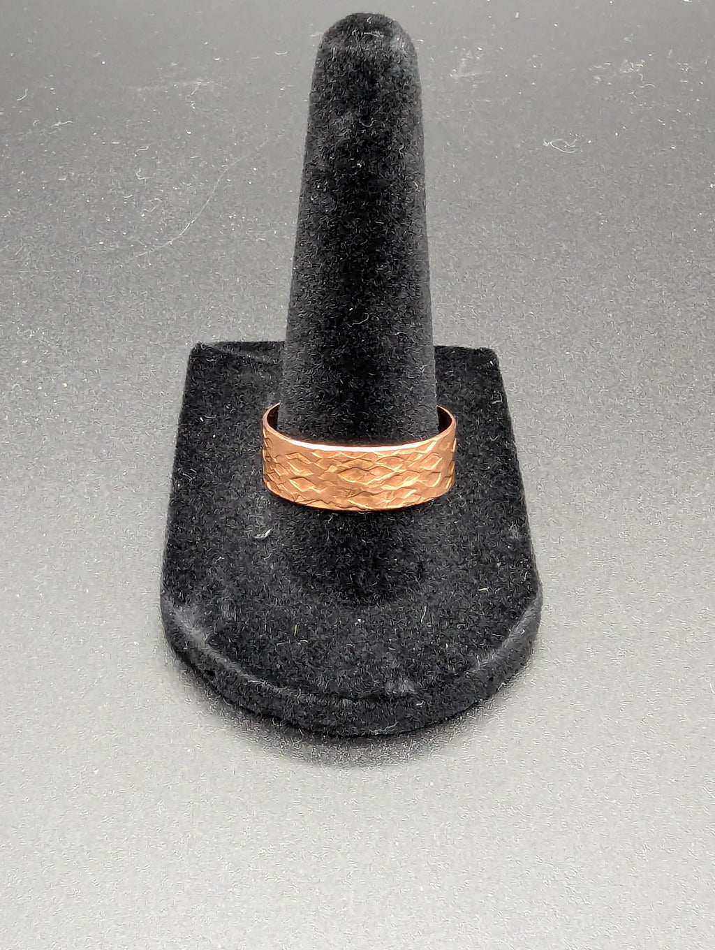 Copper ring on a black stand against a gray background. The copper ring features a striking hammered pattern resembling a snakes skin.