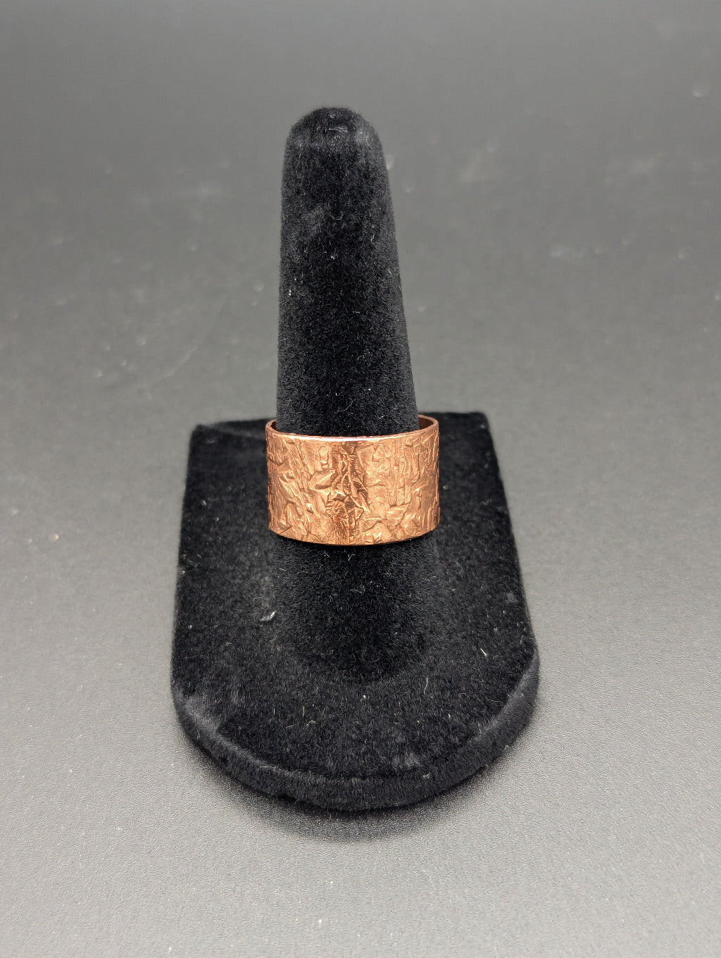 Copper ring on a black stand against a gray background. The copper ring features a striking texture that is hammered by hand.