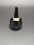 Copper ring on a black stand against a gray background. The copper ring is wrapped several times around itself.