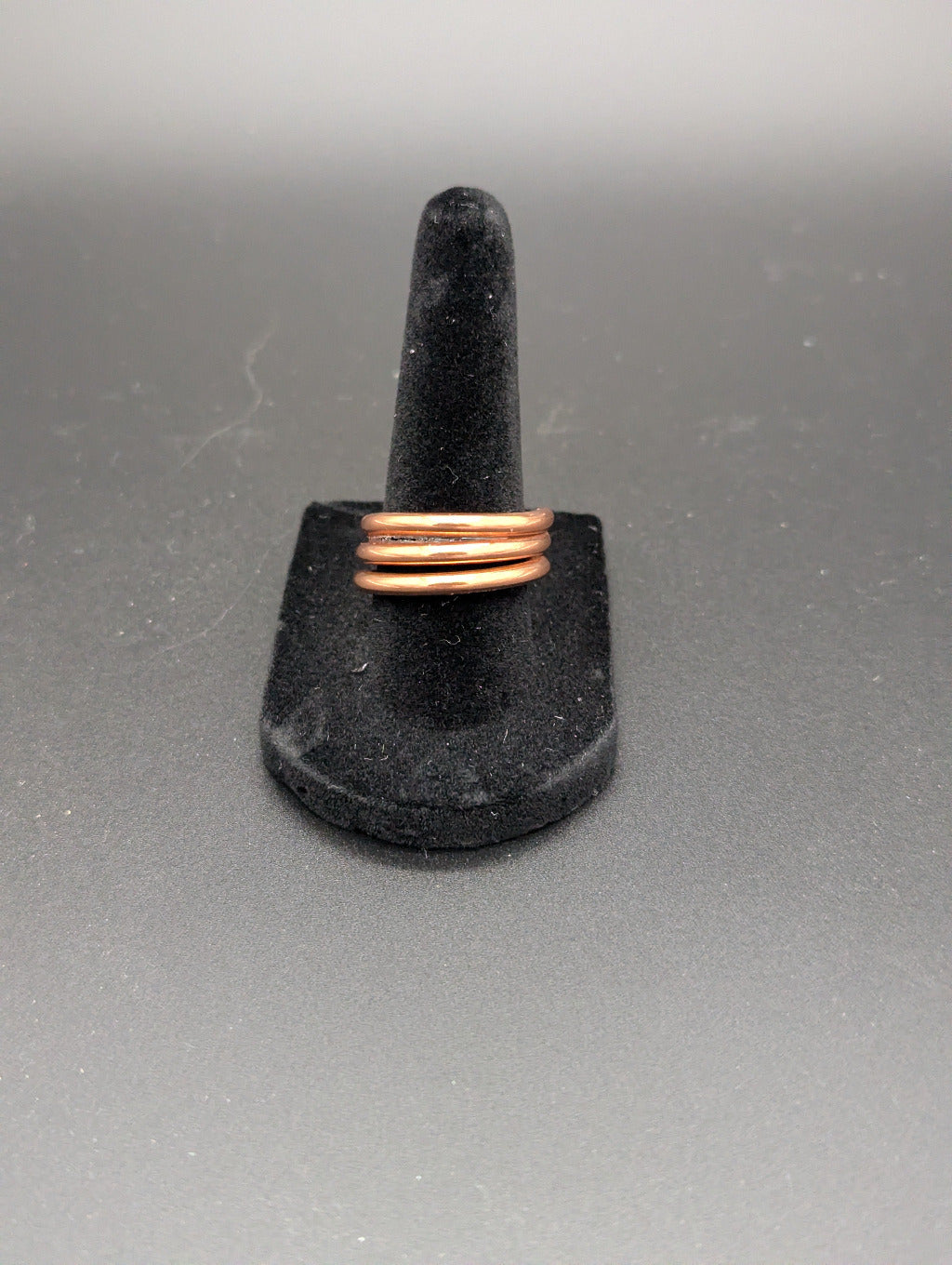 Copper ring on a black stand against a gray background. The copper ring is wrapped several times around itself.