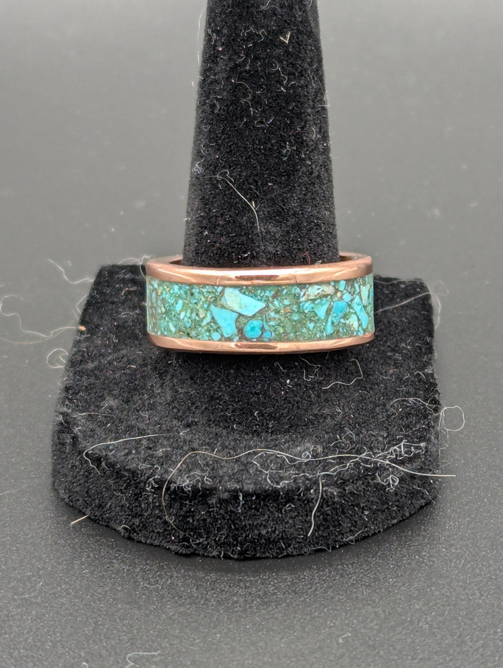 Turquoise inlay handmade copper ring on a black stand against a gray background.