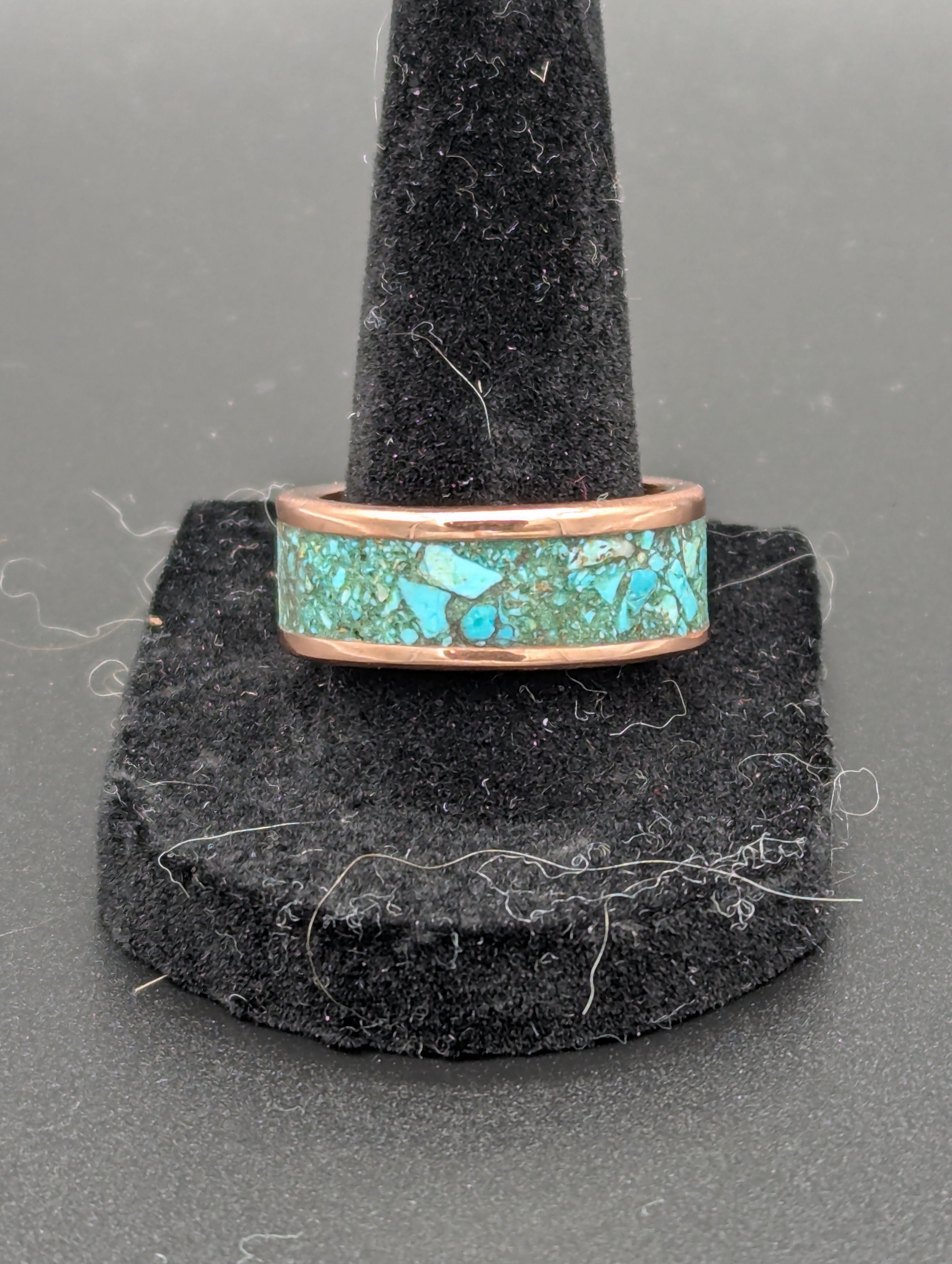 Turquoise inlay handmade copper ring on a black stand against a gray background.